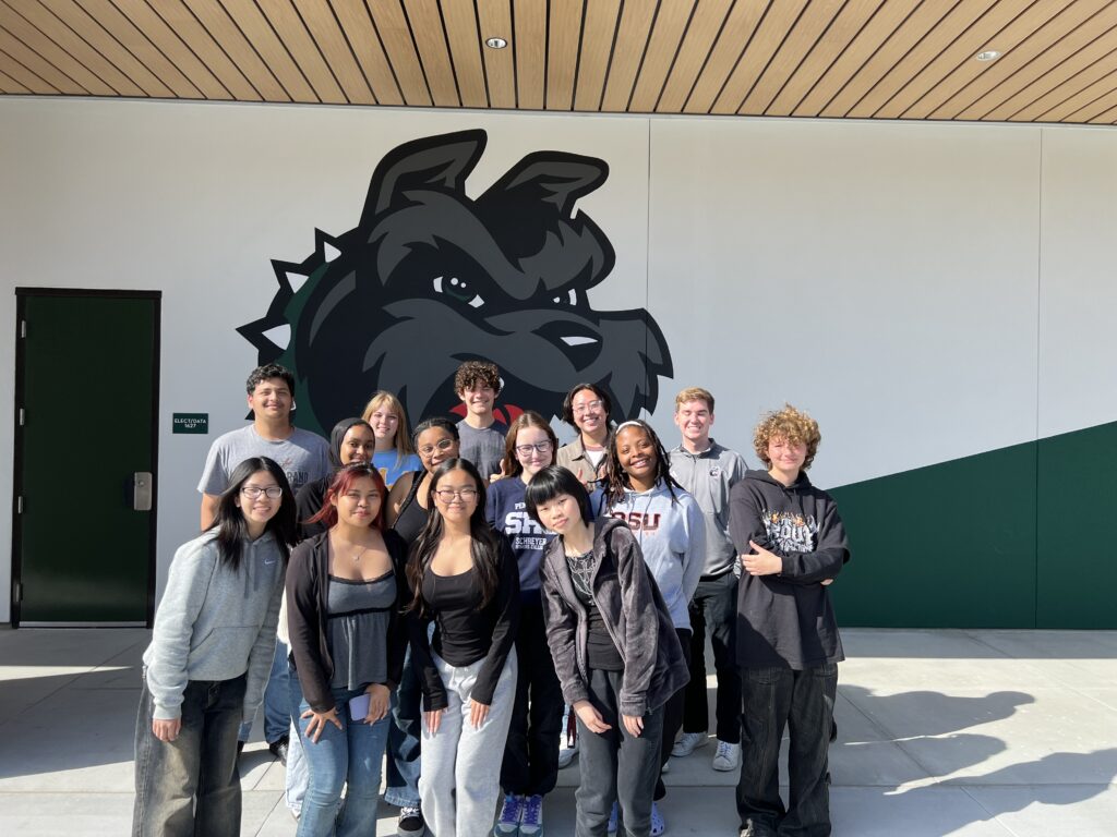 Helix Charter High School's Student Sustainability Office pose for a group photo in front of a mural of the school's mascot.
